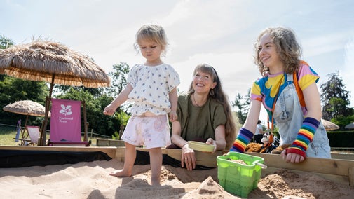 A young child playing in a sandpit with family members at Chirk Castle.